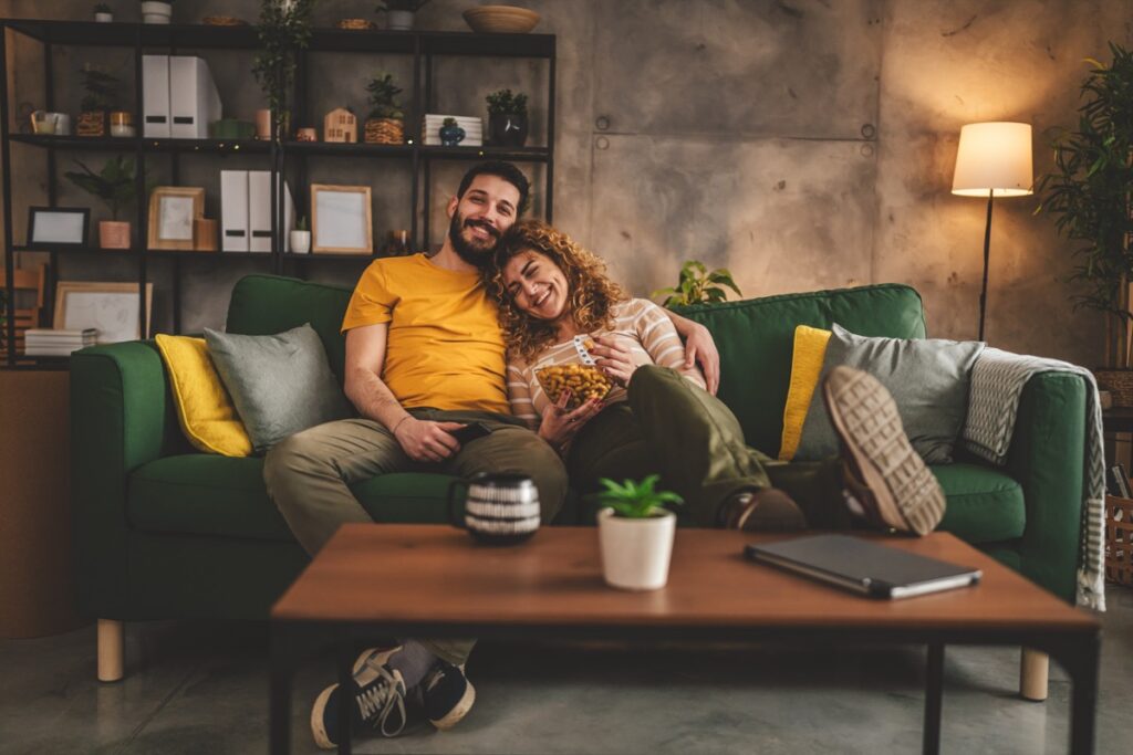 Couple man and woman caucasian husband and wife or boyfriend and girlfriend sit on the sofa bed at home watch tv movie series with hold remote controller happy smile bonding love family concept